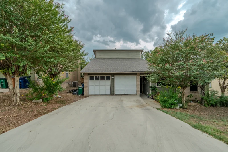 Tree-lined front exterior with a double garage and cloudy sky
